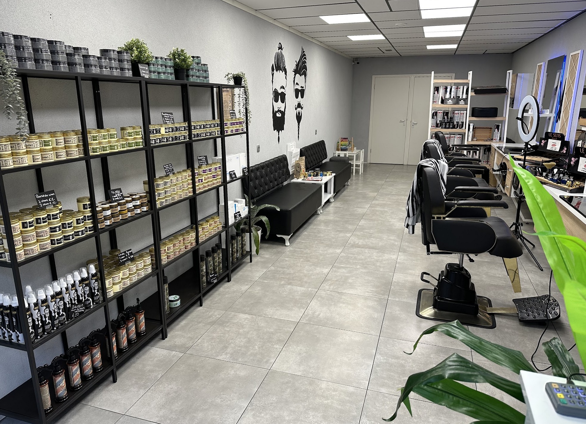 Het interieur van Haarstudio B: links een lange wand met schappen vol haarproducten, rechts een rij zwarte kappersstoelen