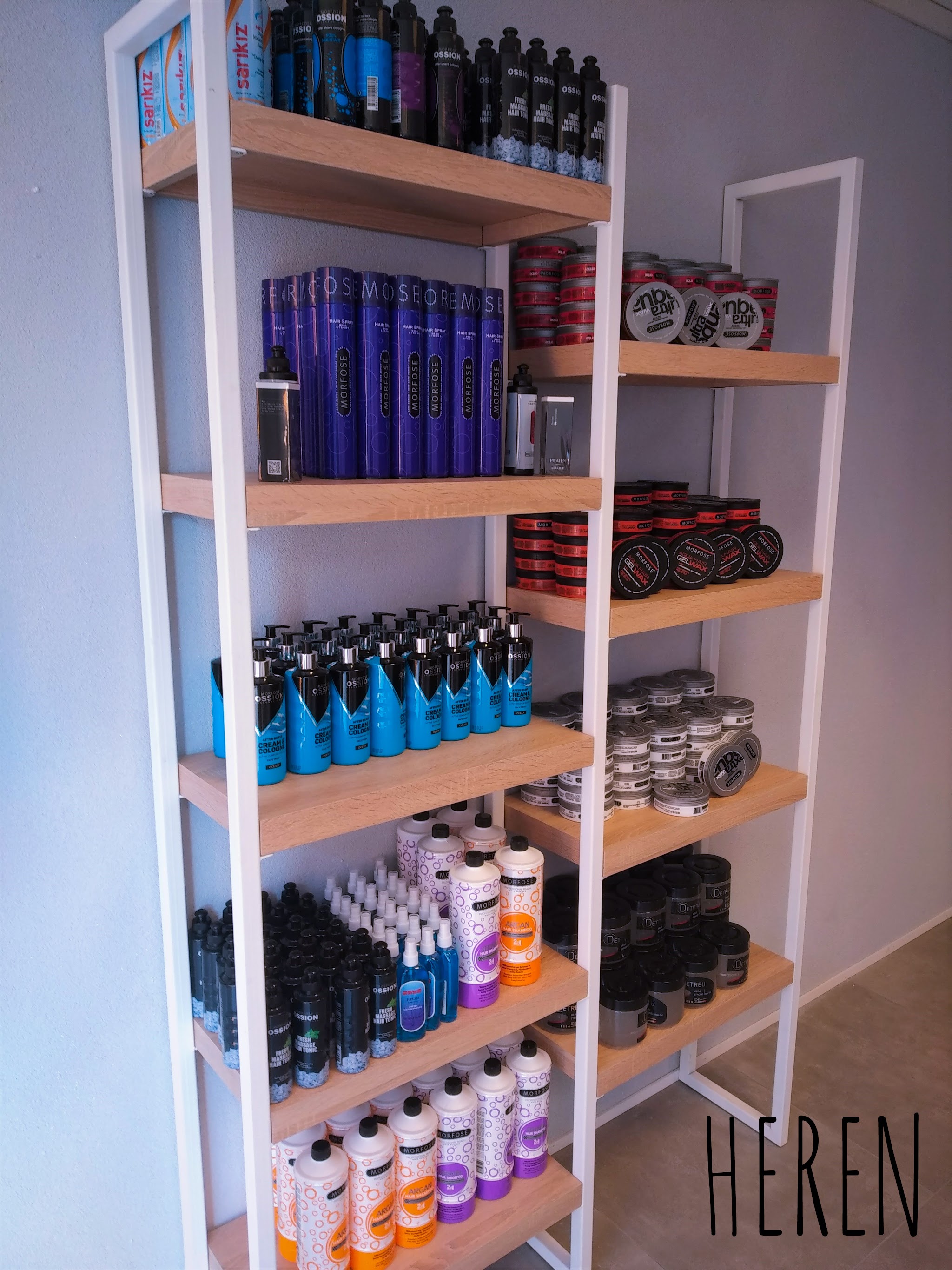 Een witte kast met houten planken vol haarsprays, styling en verzorging, met het woord HEREN op de muur